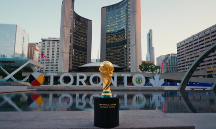 FIFA World Cup trophy displayed in front of the city's iconic illuminated "Toronto" sign and modern architecture at dusk