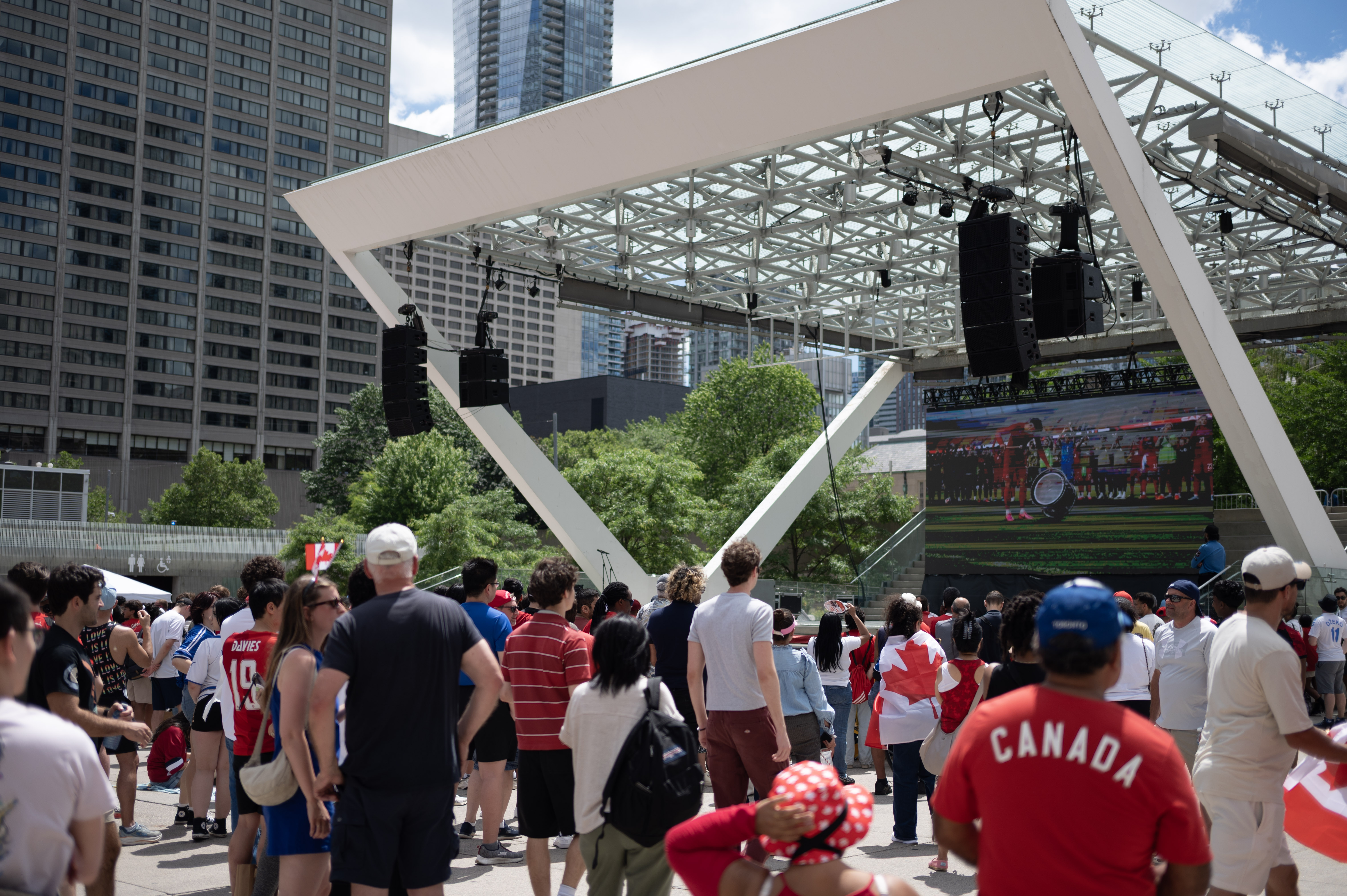 People watching soccer on a large outdoor screen in a public square.