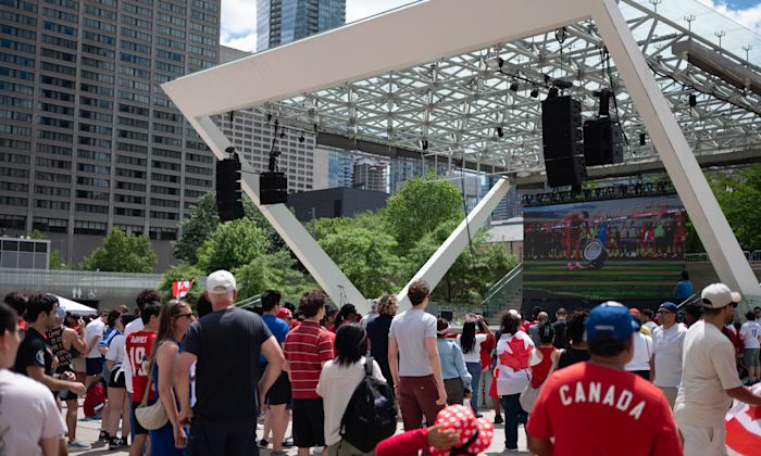 People watching soccer on a large outdoor screen in a public square.