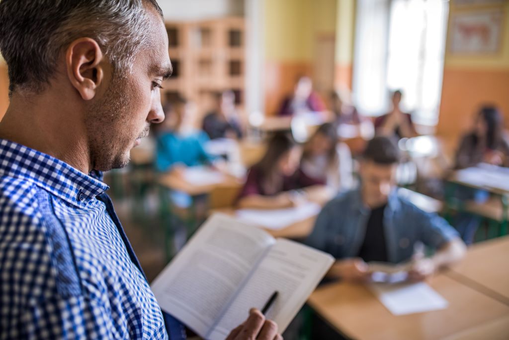 an instructor reading a textbook in front of his class of students