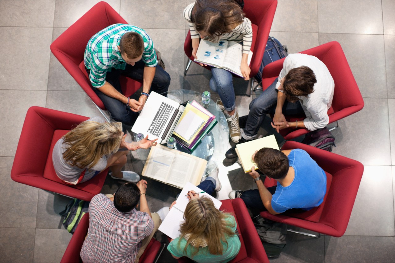 a group of students sitting in a circle asking questions and conversing in a contemporary university library settings