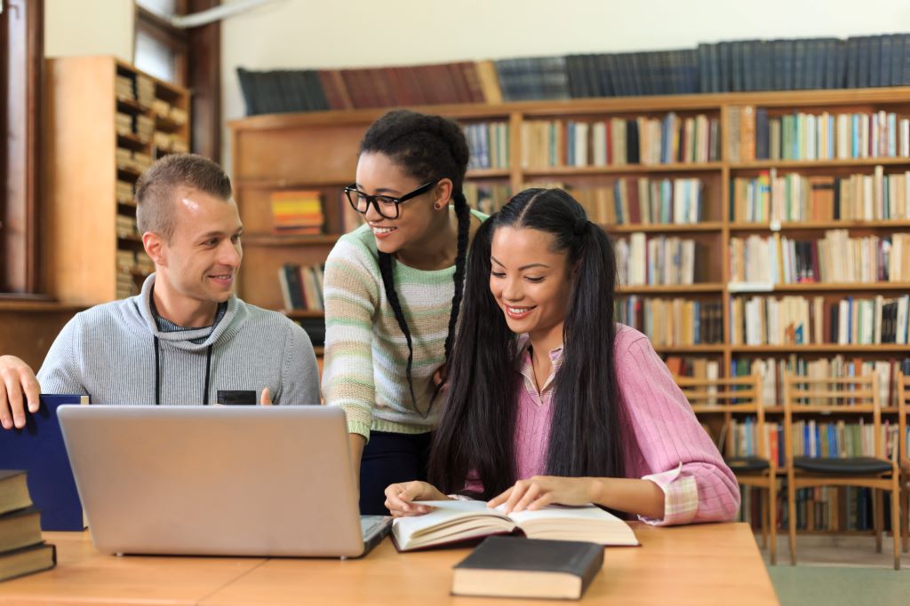 two students in a library, a librarian is standing nearby to help them.