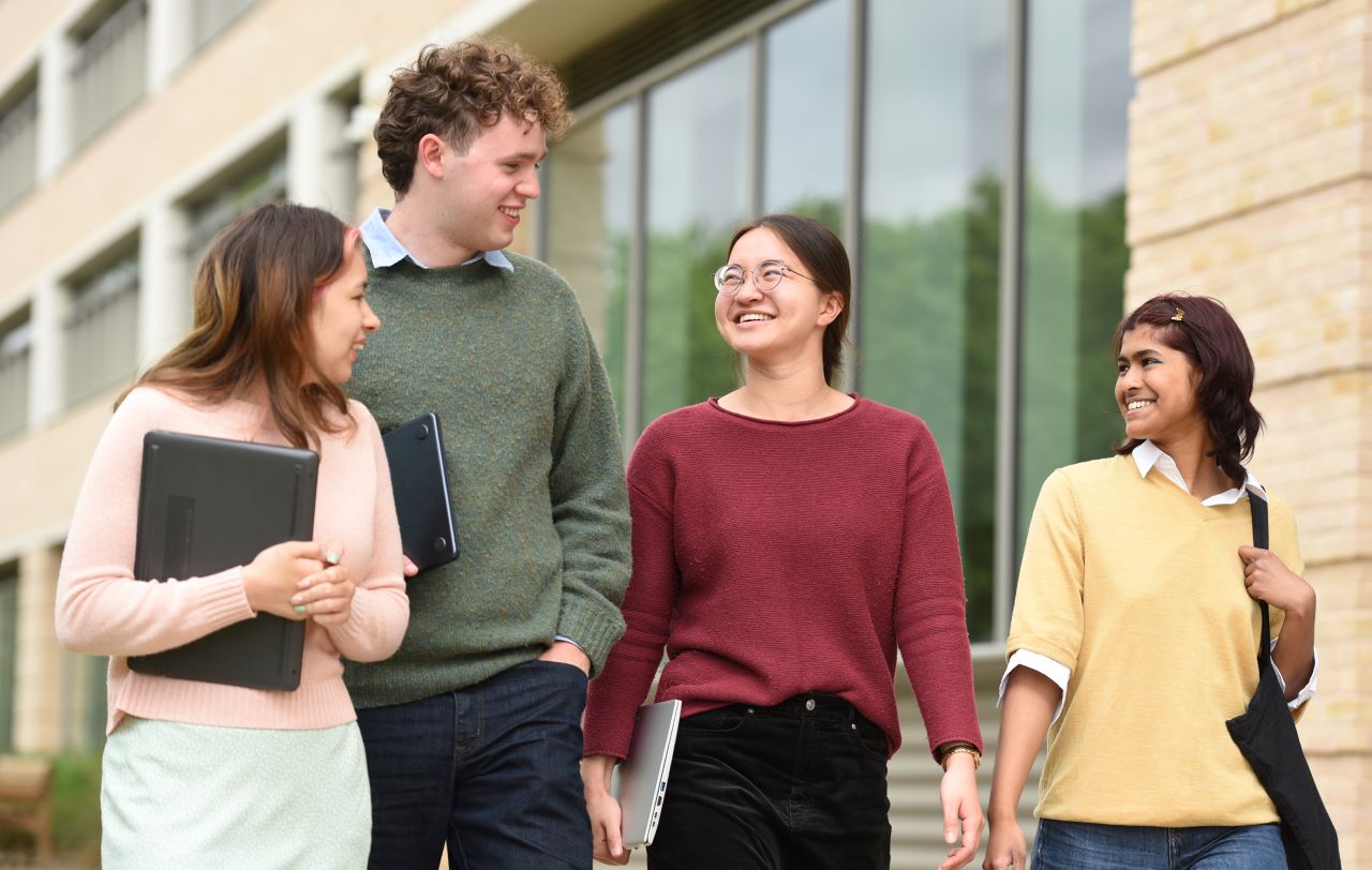 A group of higher education students walking outside, they look happy and friendly.