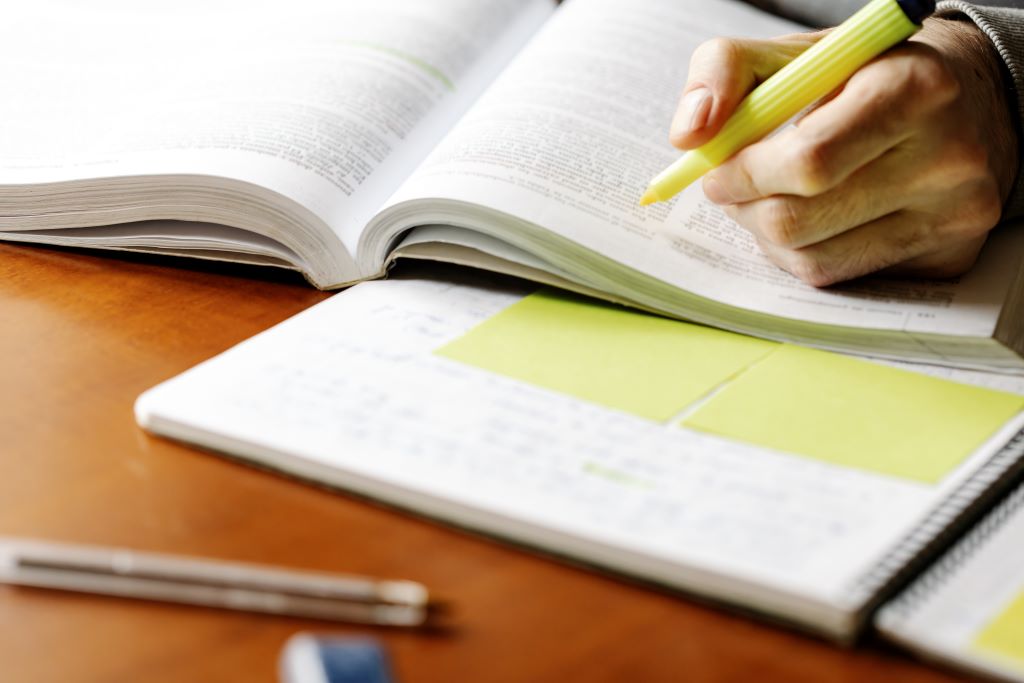 A close-up photo of a book, a hand holding a highlighter scans the page to highlight important passages.