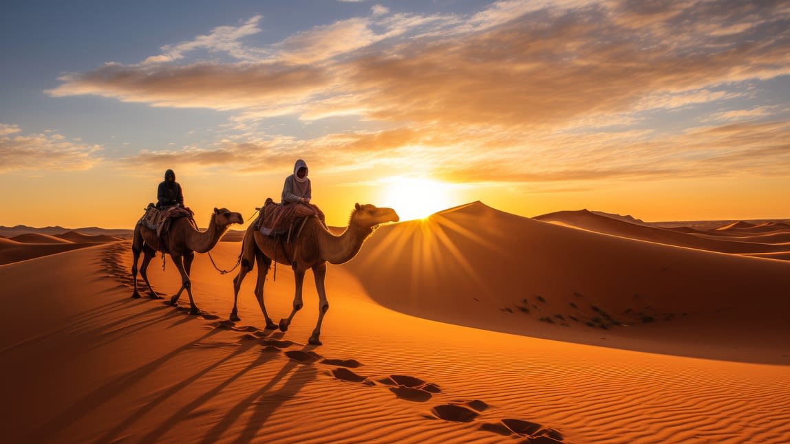 Image of a desert, with two people walking two camels. 