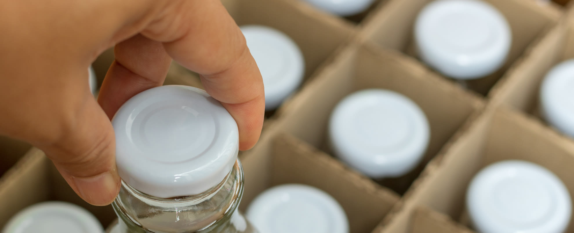 The hand picking a glass bottle with white bottle caps in a cardboard box, Packaging concept.