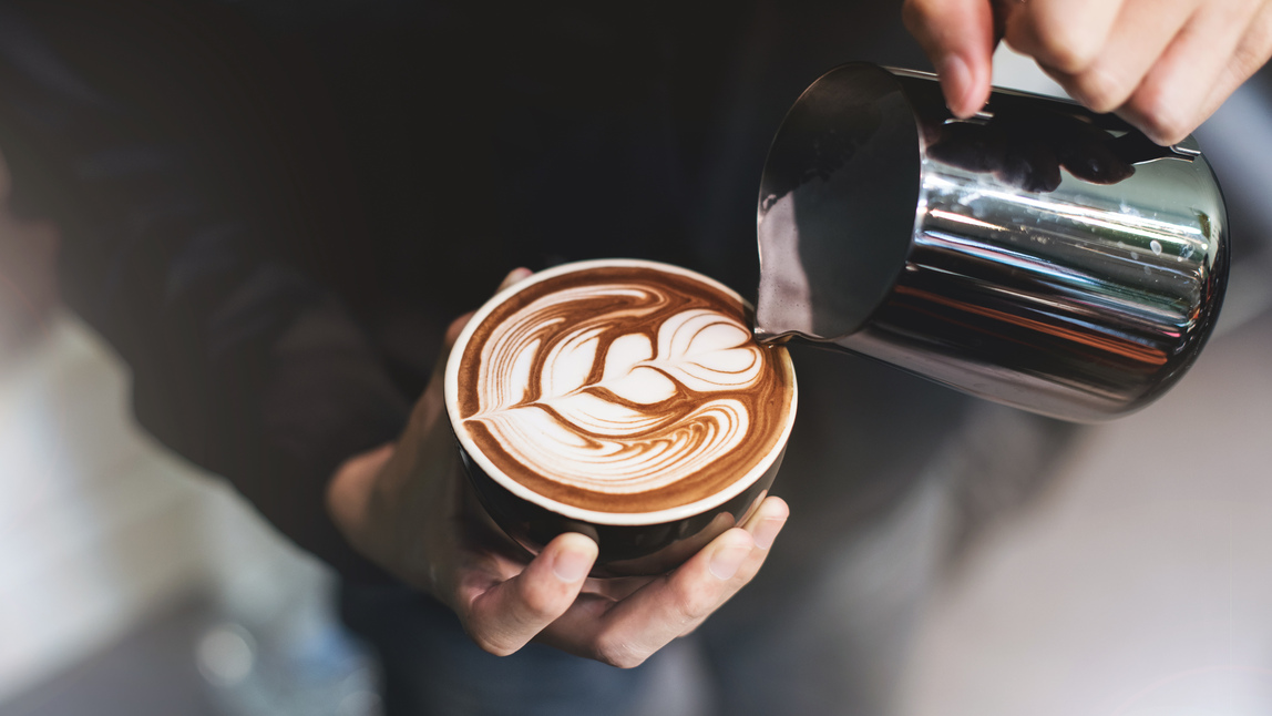 Milk from a steaming jug being poured into a cup of coffee to make latte art. 