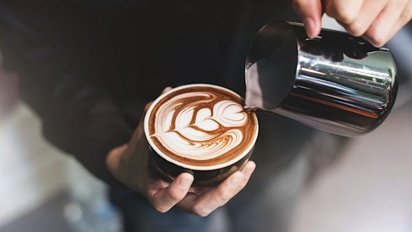 Milk from a steaming jug being poured into a cup of coffee to make latte art.