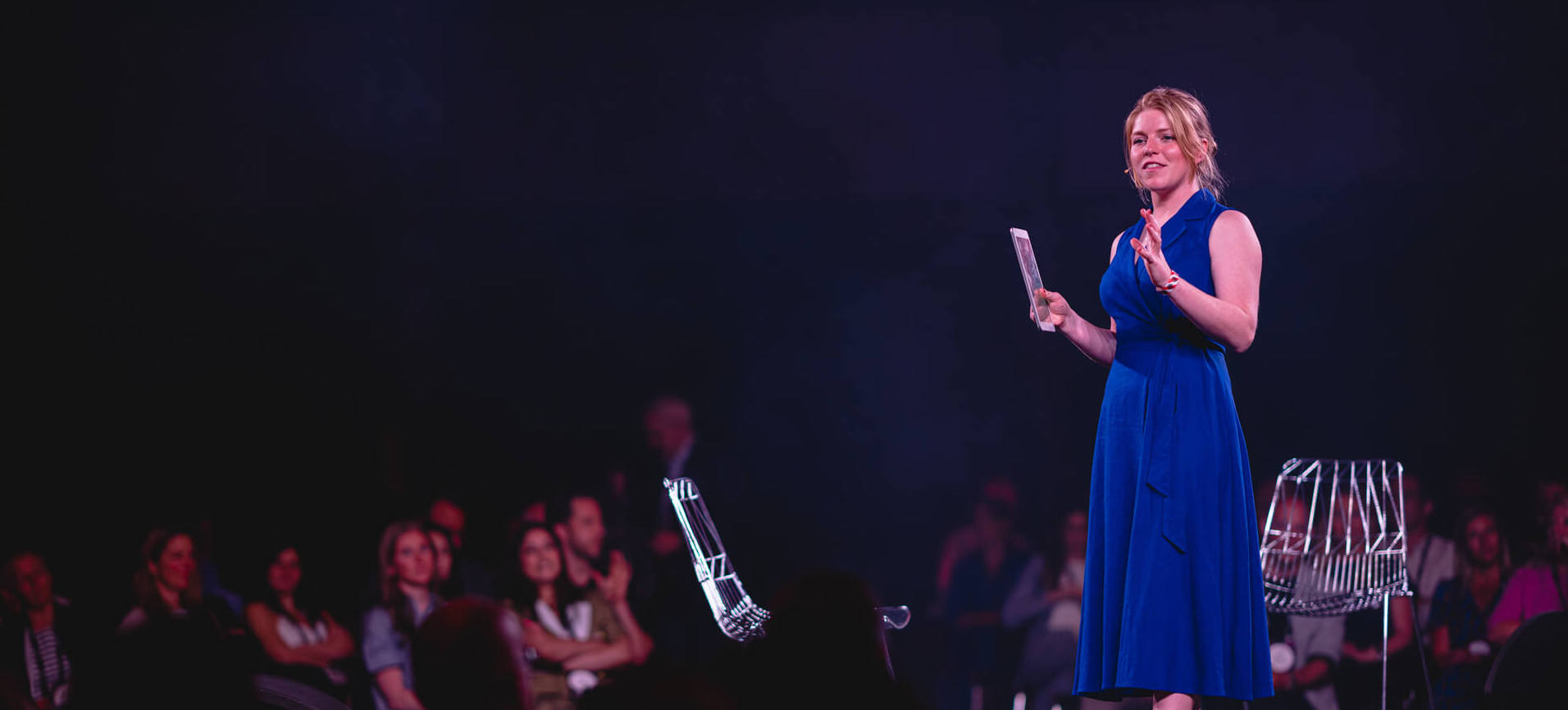 Person talking on stage with audience in the background