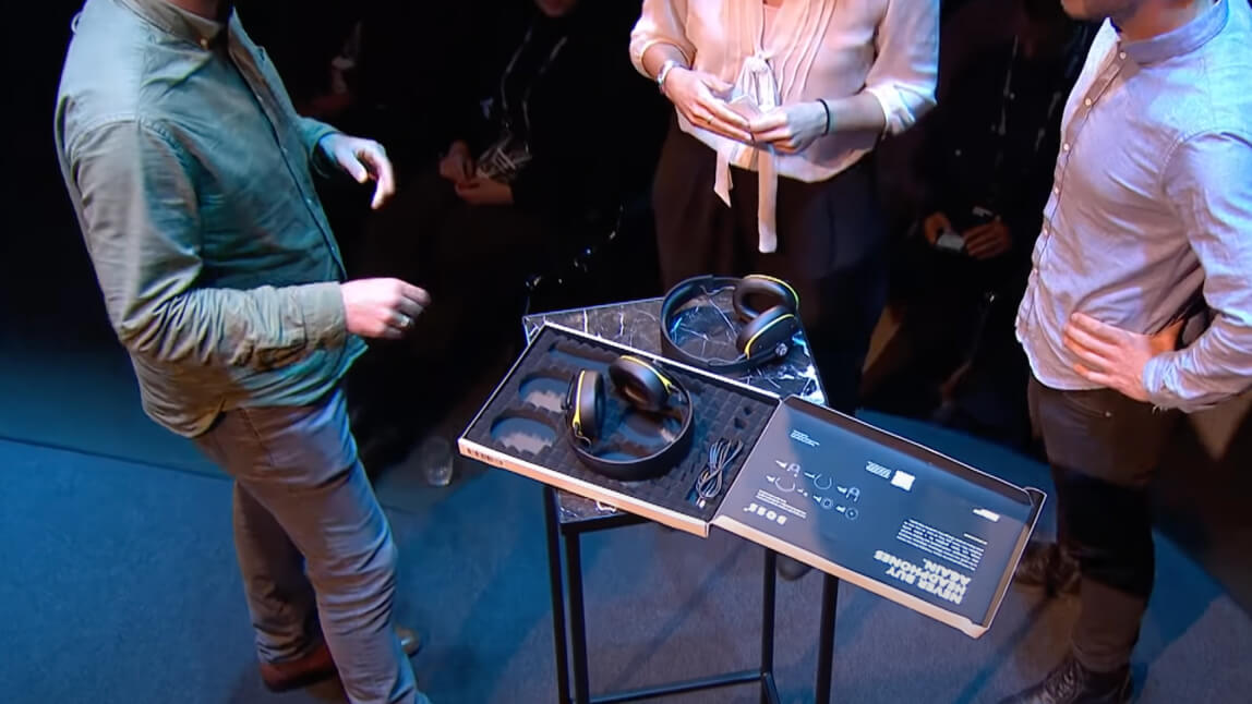 headphones on a table with people stood around talking