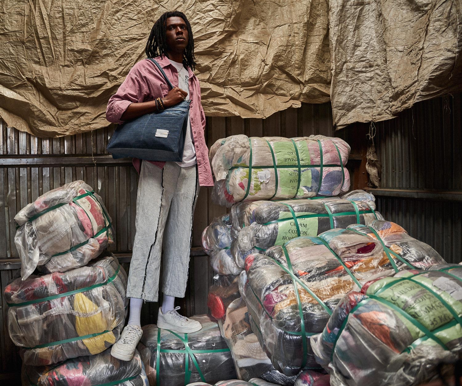 An African man standing with a bag stood next to big packages of reused material