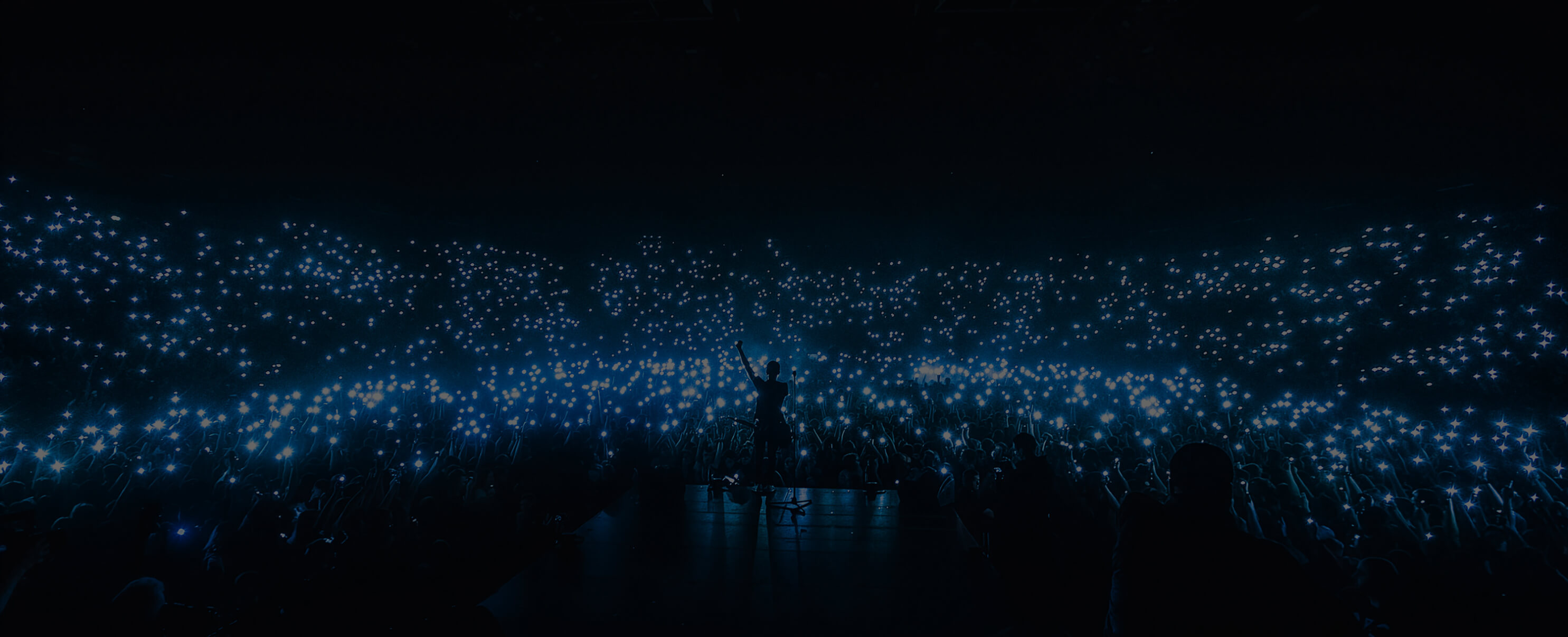 Phone lights being waved in the air at a concert by the crowd