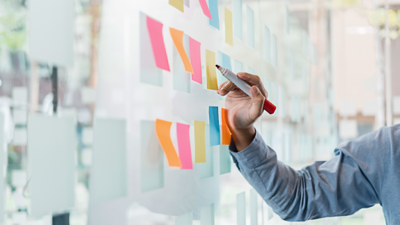 Person drawing on acrylic board with post it notes