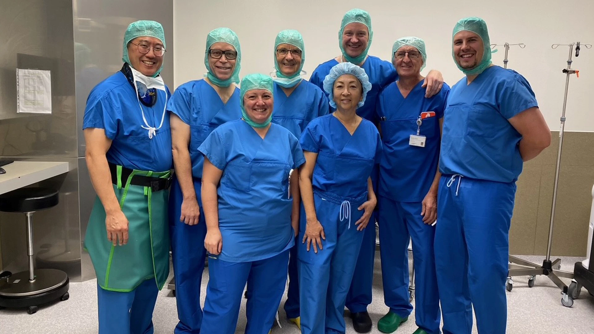 Dr. Kelly (left, bottom row) posing for a photo in the OR with Beat Hintermann, MD (third from left, top row), Roxa Ruiz, MD (right, bottom row), and their team in Basel, Switzerland.