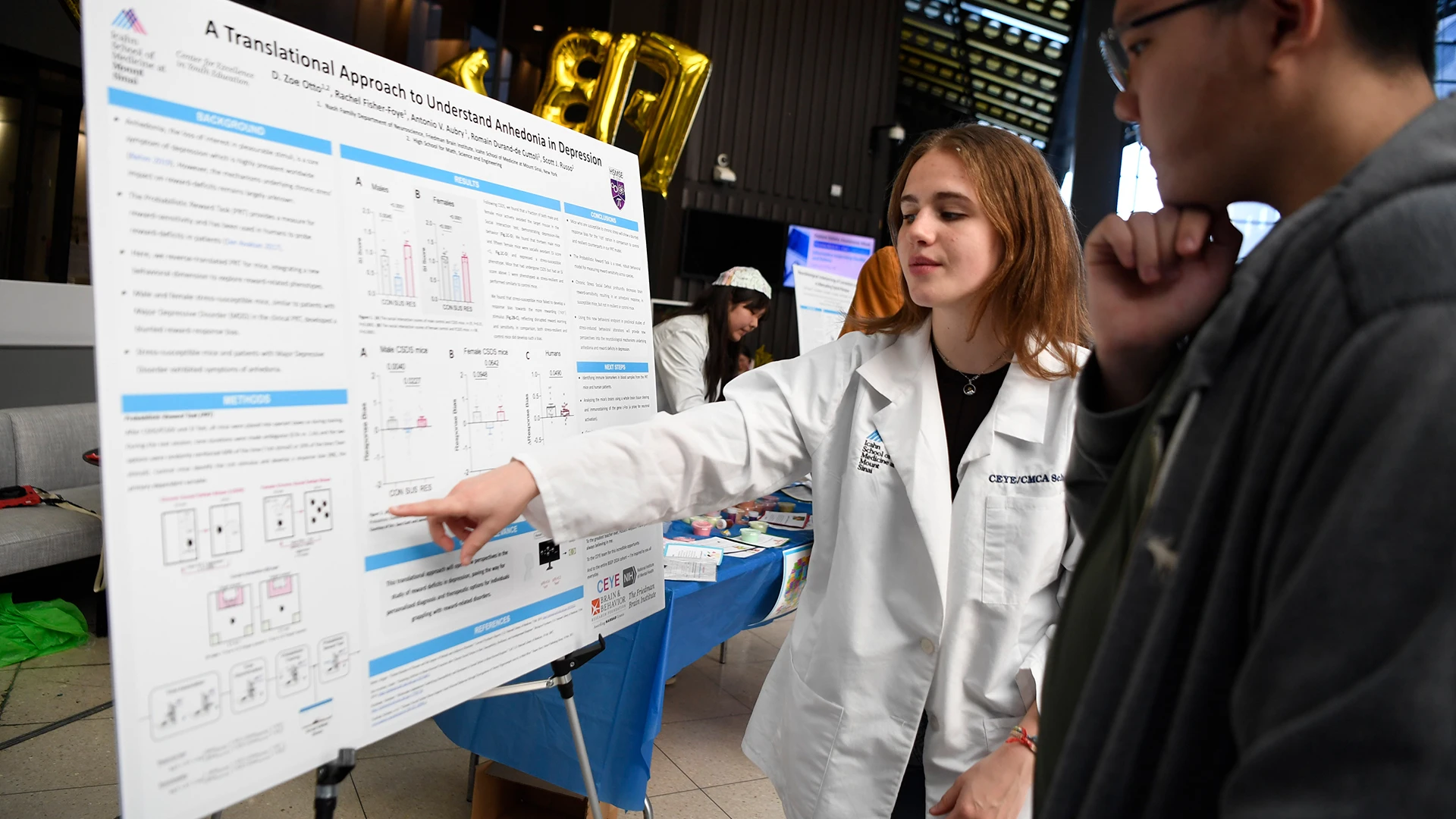 High school junior Zoe Otto at The Friedman Brain Institute Brain Fair explaining a lab research project to Oliver, also a junior. 