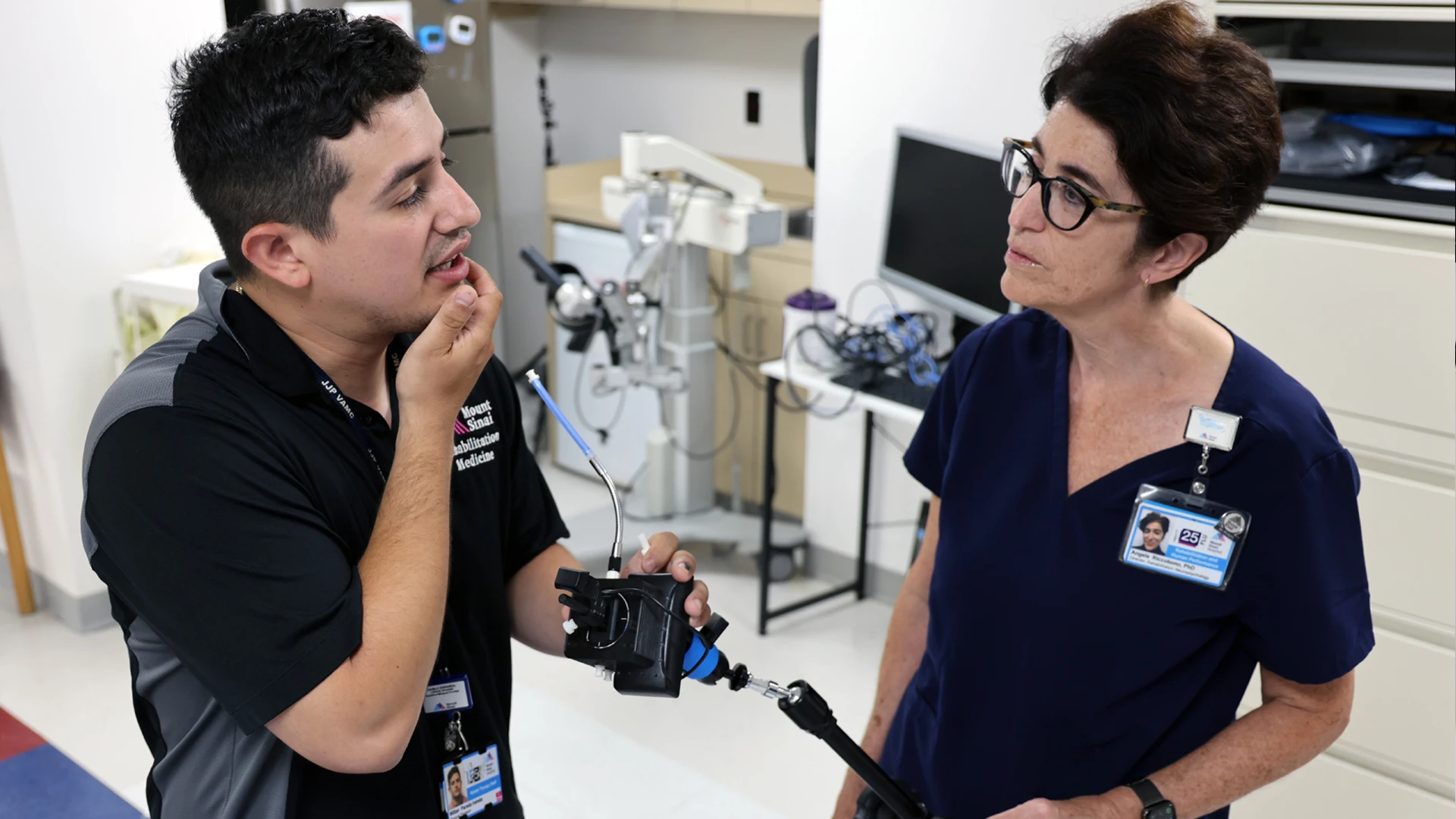 Technology has advanced these adaptive controllers and setups to a point that people with spinal cord injuries using them perform just as proficiently as other people on regular keyboards and controllers, said Wilber Parada Iraheta, DPT, Lead Physical Therapist (left) at the Abilities Research Center at Mount Sinai. These setups can be customized to the level of need of the patient, he said, demonstrating to Angela Riccobono, PhD, Associate Professor Rehabilitation and Human Performance (right), how the chin supports of the mouth stick controller can be adjusted.