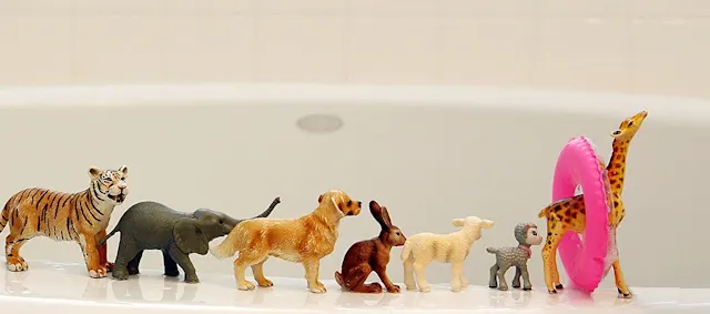 plastic animal toys lined up on the edge of a bathtub