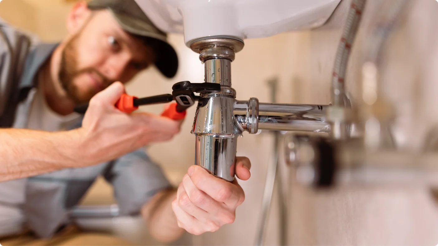 plumber using adjustable wrench to remove pipe underneath sink