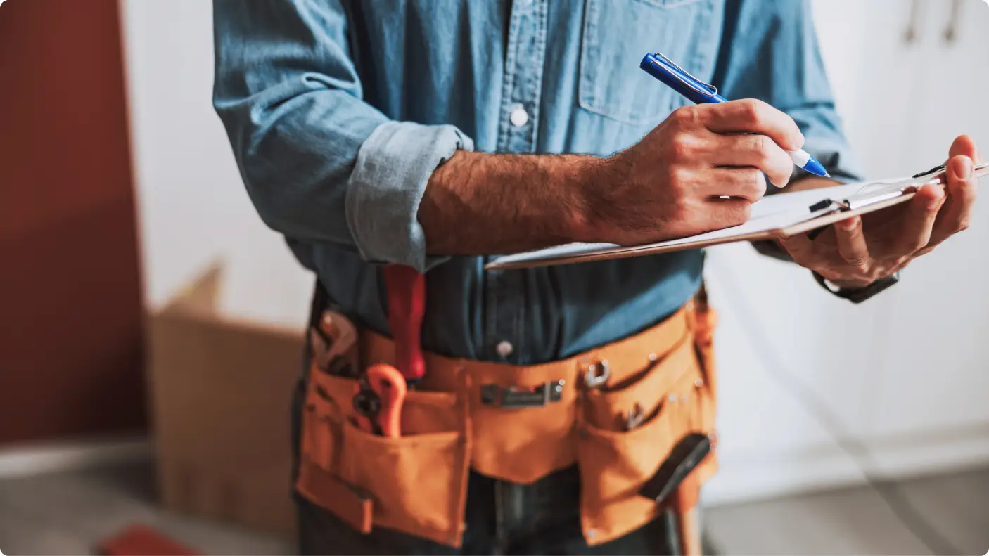 contractor with tool belt around waist and clipboard in hand marking maintenance list