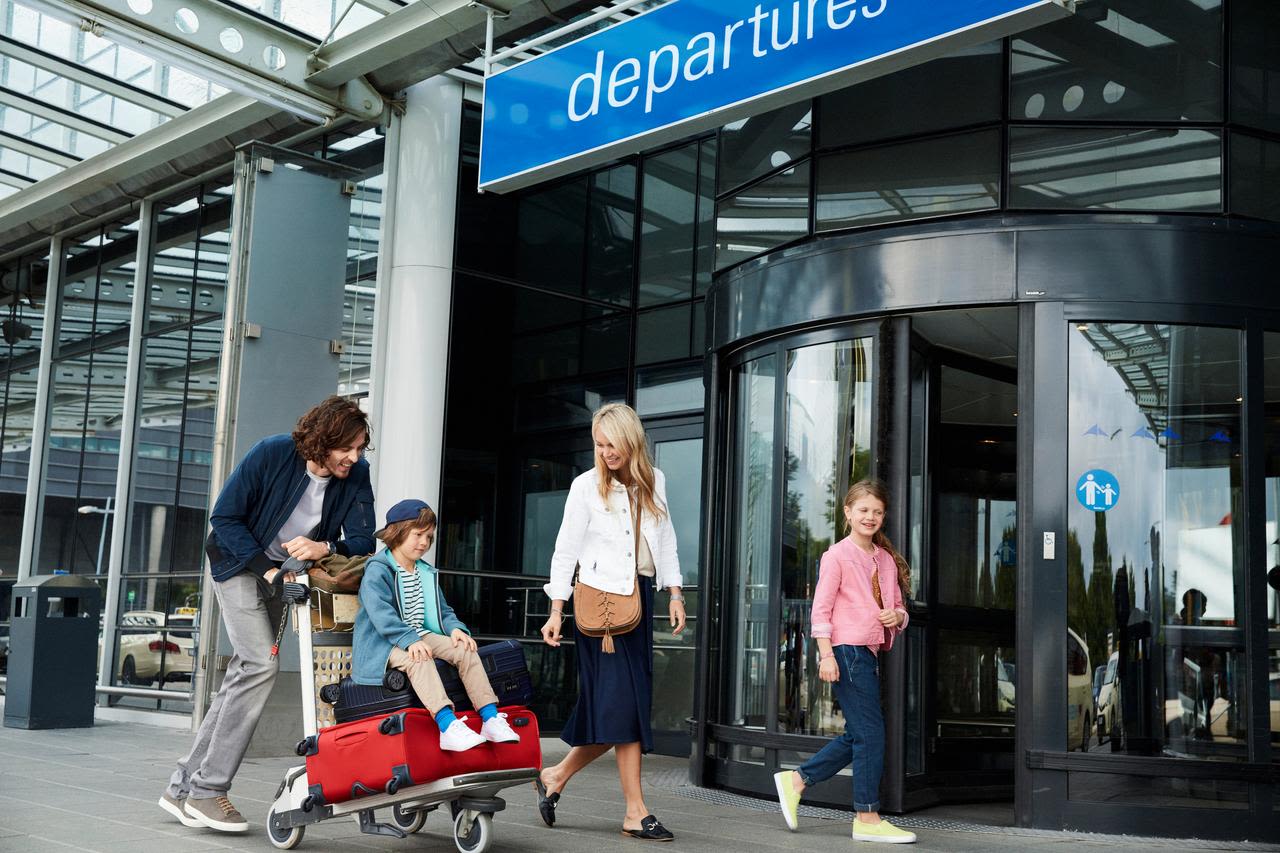 Flughafen Eingang Familie mit zwei Kindern und Koffertrolley am Eingang zur Abflughalle am Flughafen