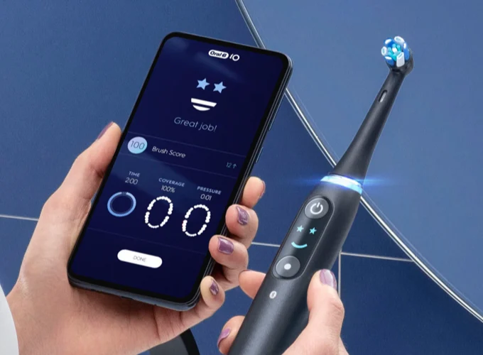 Oral-B app on phone and black Oral-B iO electric toothbrush with smiley face on LCD screen