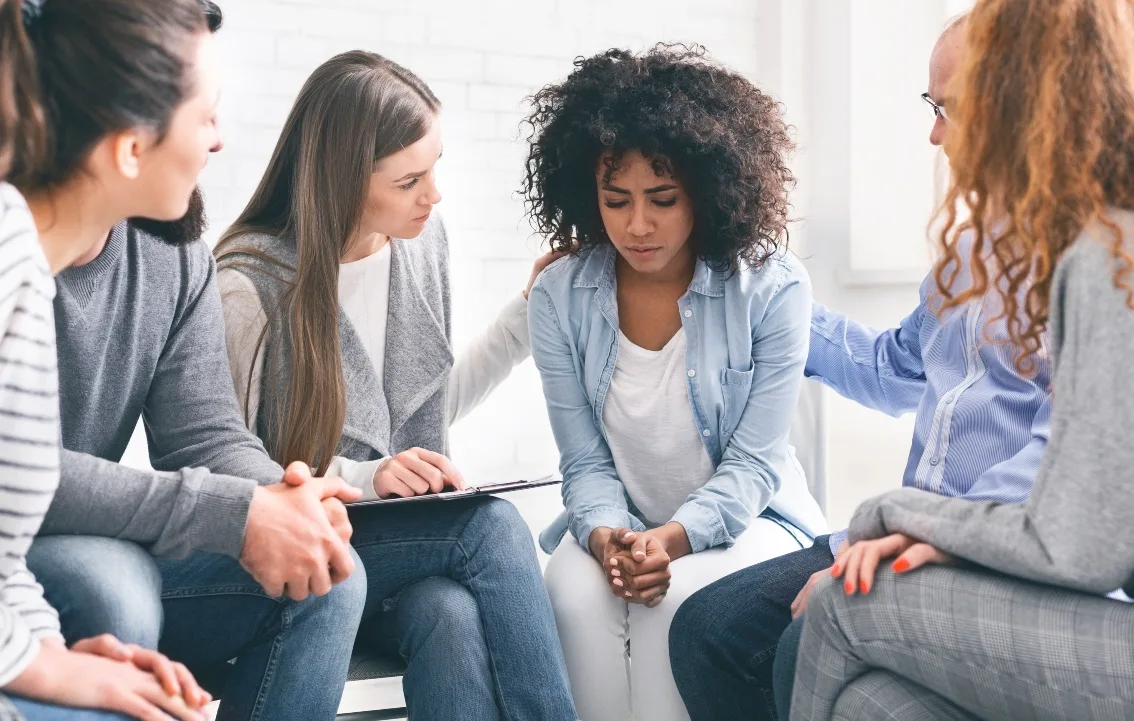 Woman talking to people sitting in a circle around her comforting her 