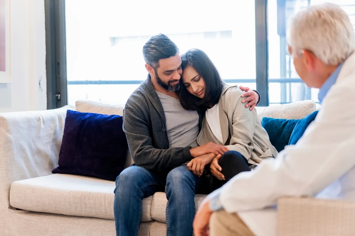 Sad couple on couch speaking to doctor