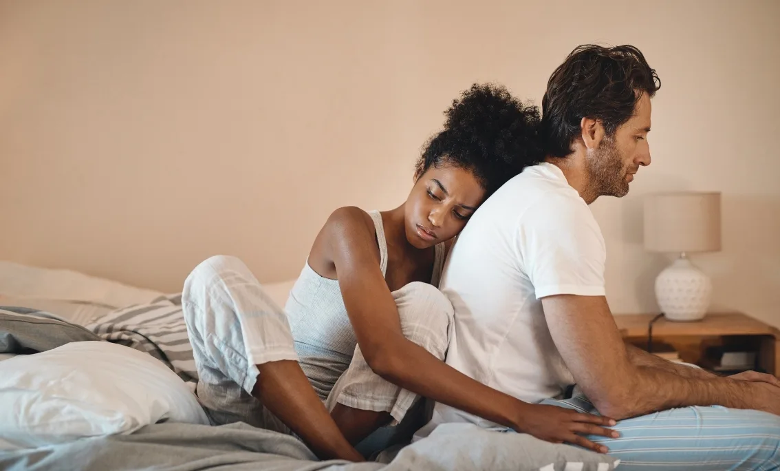 Black woman on bed with her arms around a man looking sad 