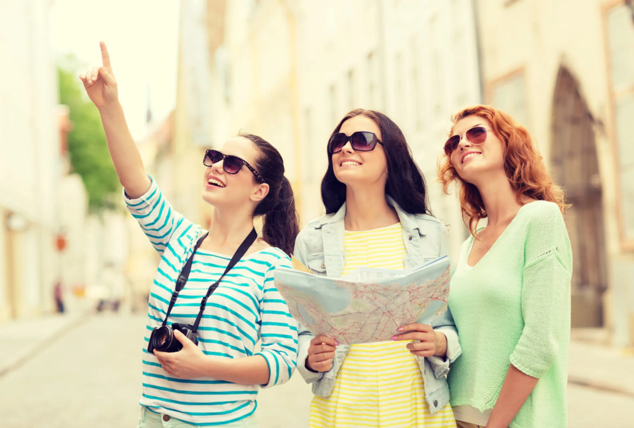 smiling teenage girls with map and camera outdoors