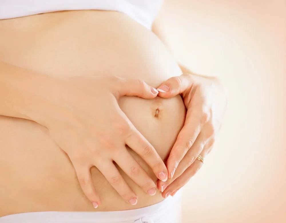 Pregnant Woman holding her hands in a heart shape on her baby bump.