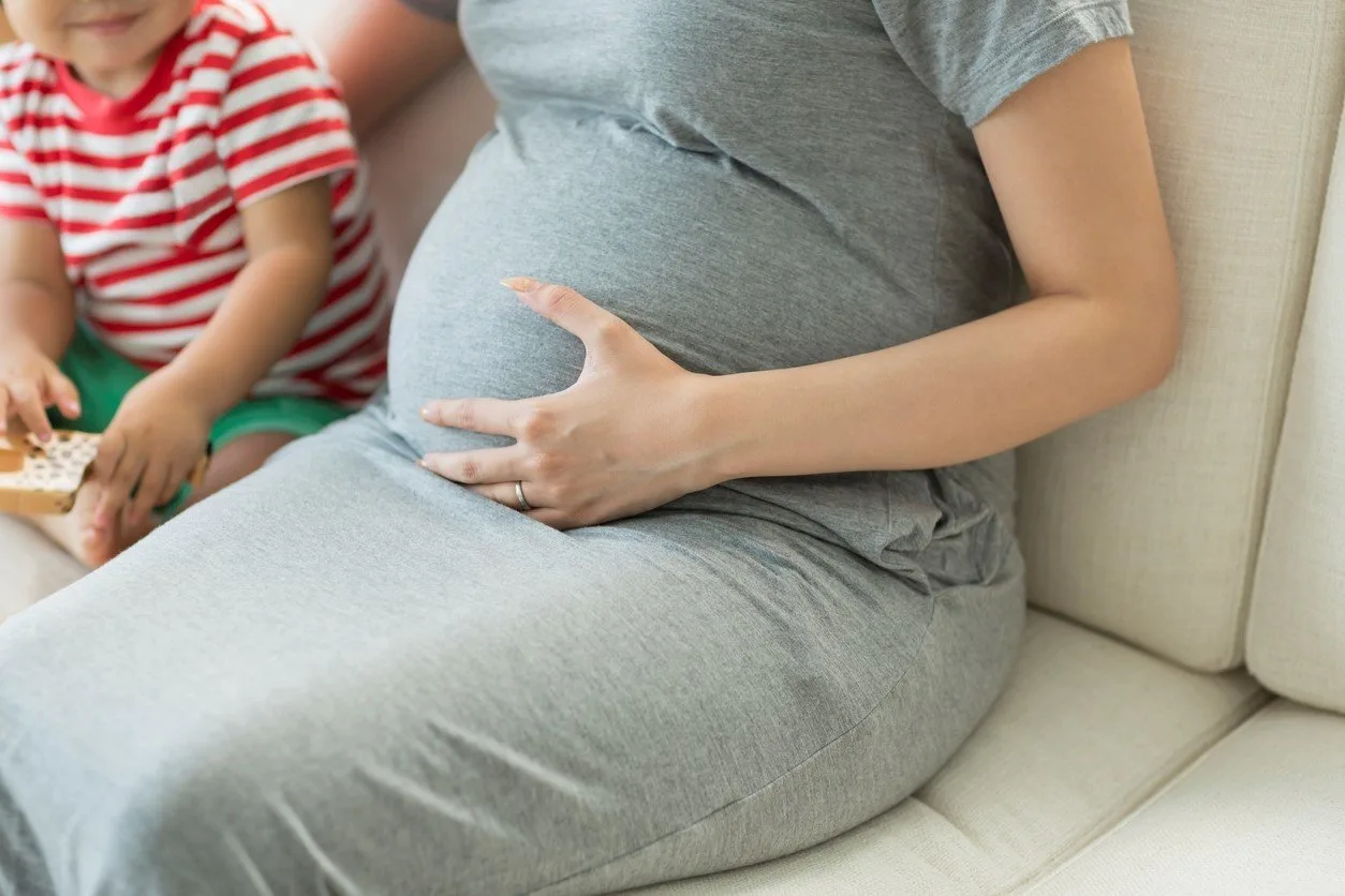 mom holding pregnant belly beside child