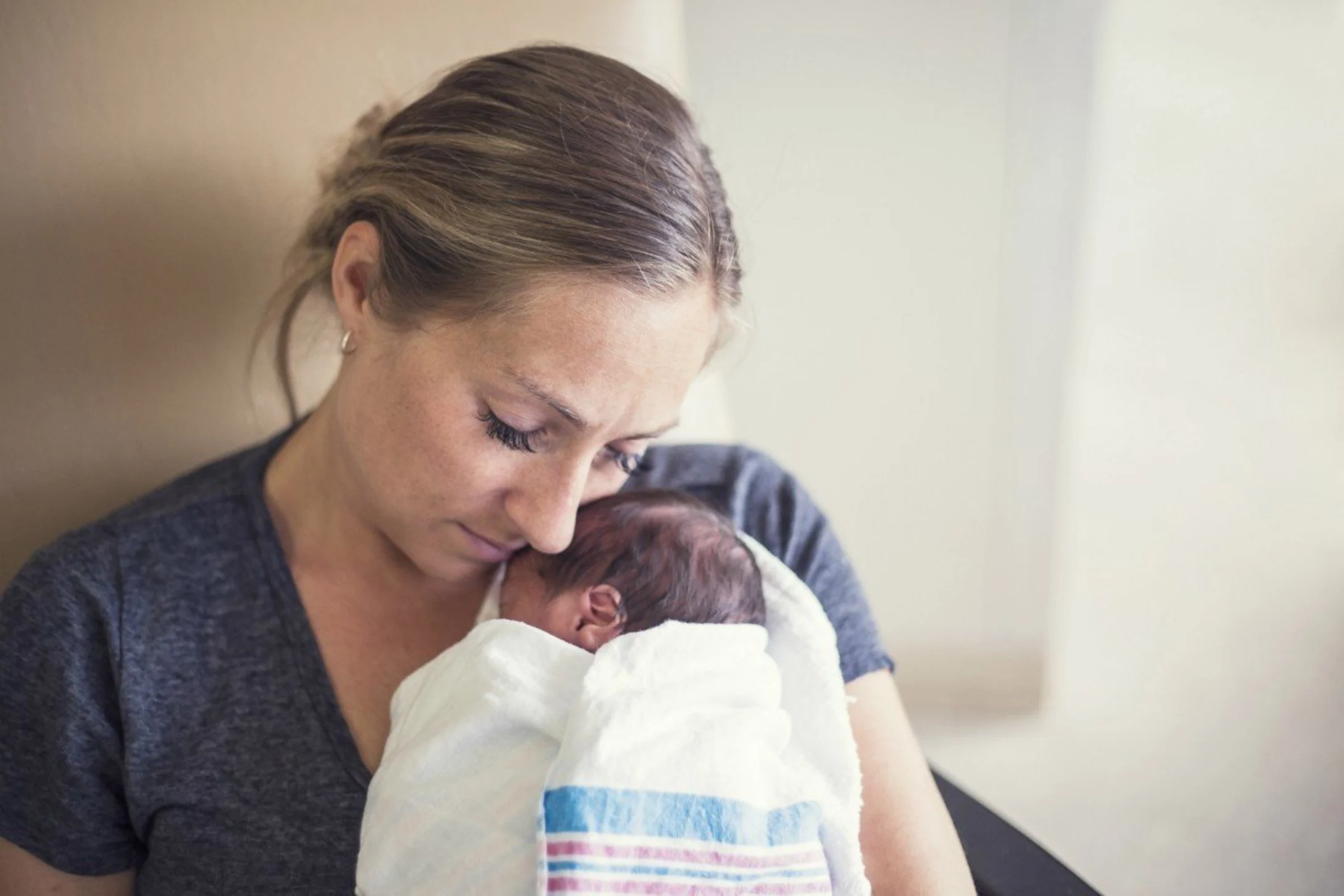 A mom sits in a chair in the NICU ward, gently cradling her baby close.