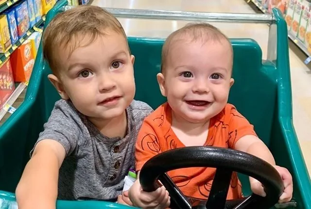 Two toddler boys smile while sitting in a shopping cart