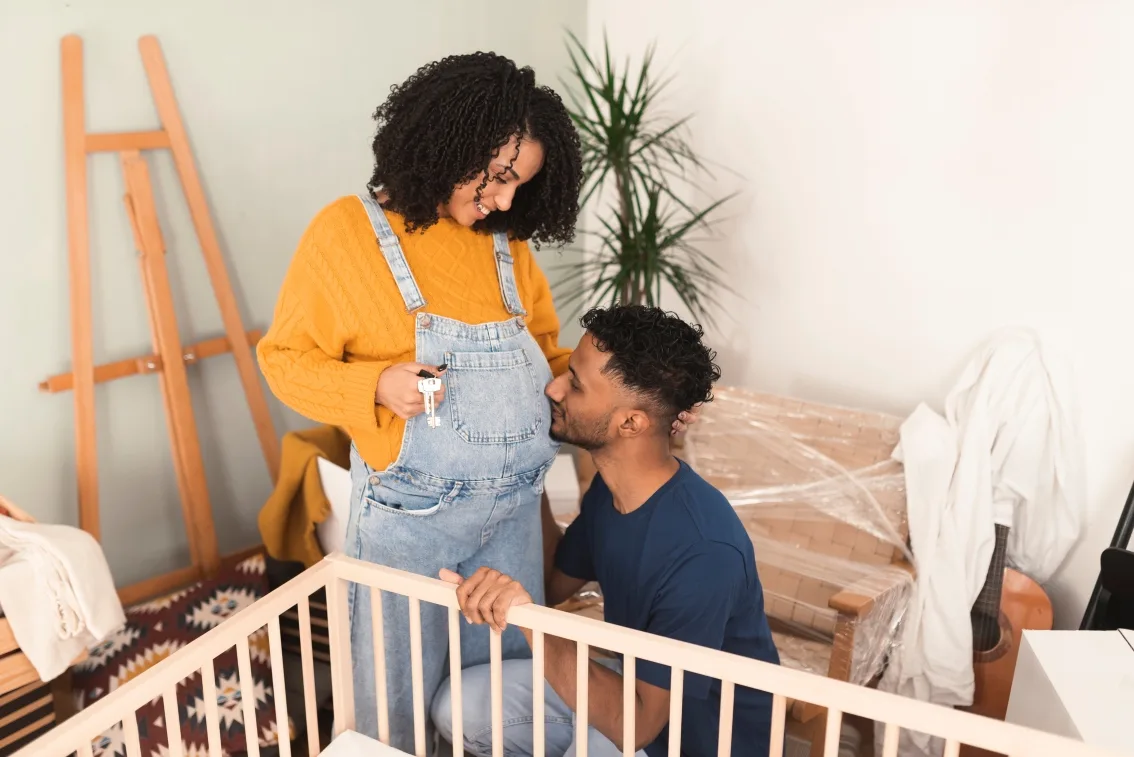 Dad-to-be kisses partner's pregnant belly as they set up the nursery