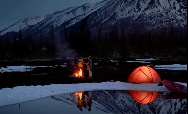 Naturbilde tatt i mørket, telt og fjellandskap som speiler seg i et vann.