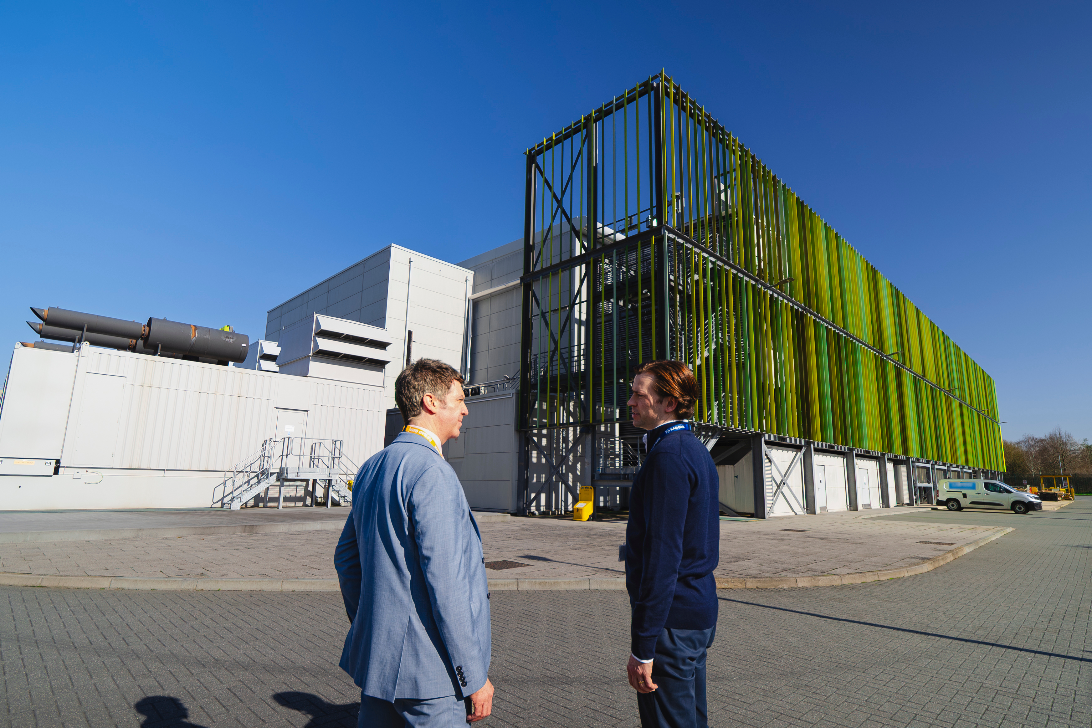Two men speaking outside in front of a grey and green data center.