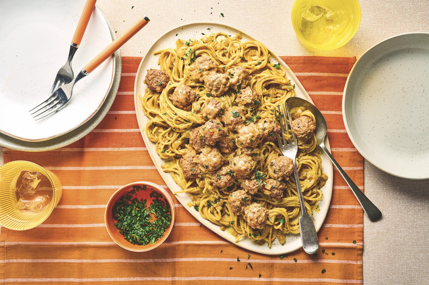 Overhead view of meatballs, noodles and herbs on a striped mat.
