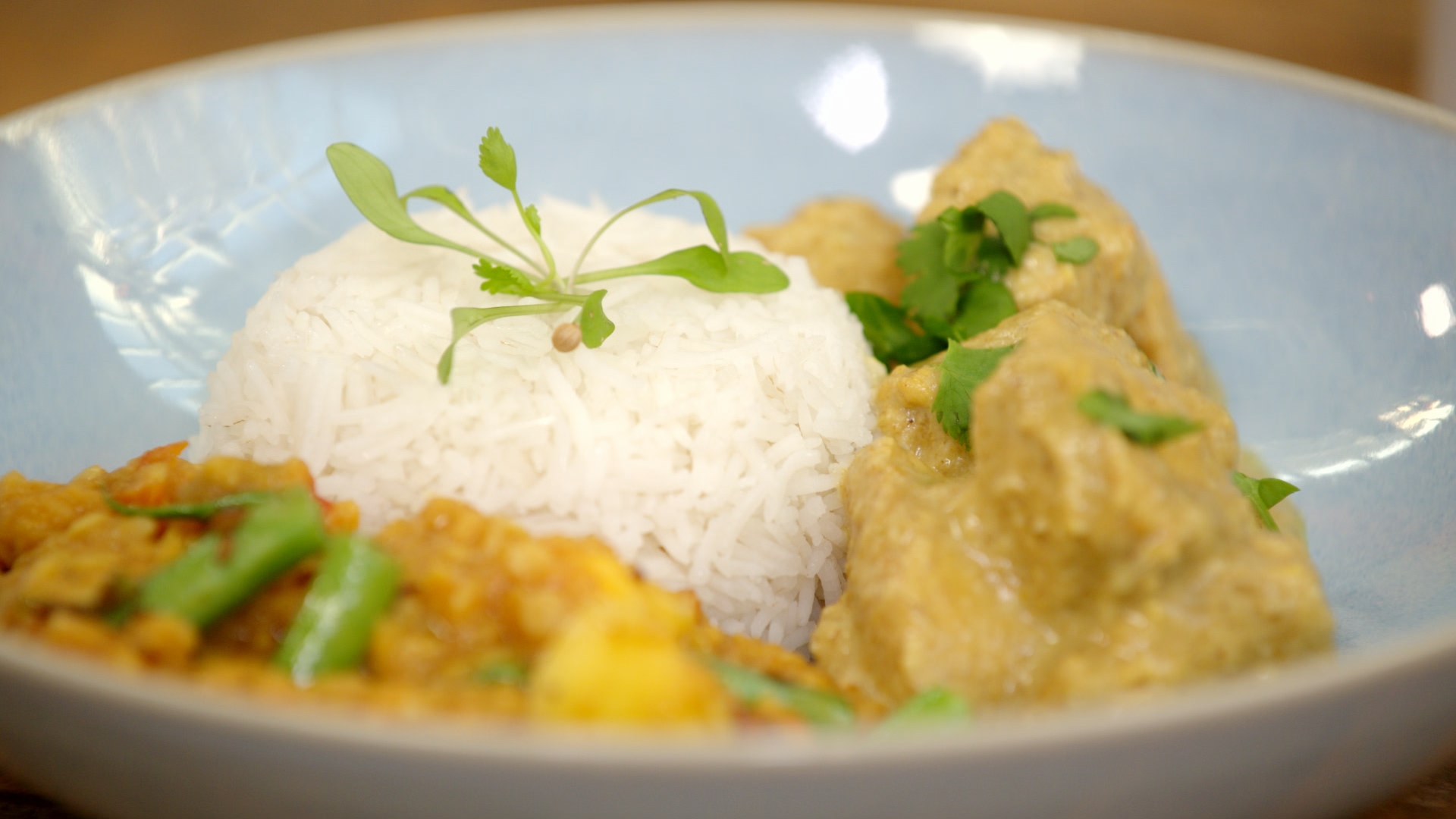 White rice mound garnished with microgreens on a blue plate, accompanied by curry dishes with fresh coriander.