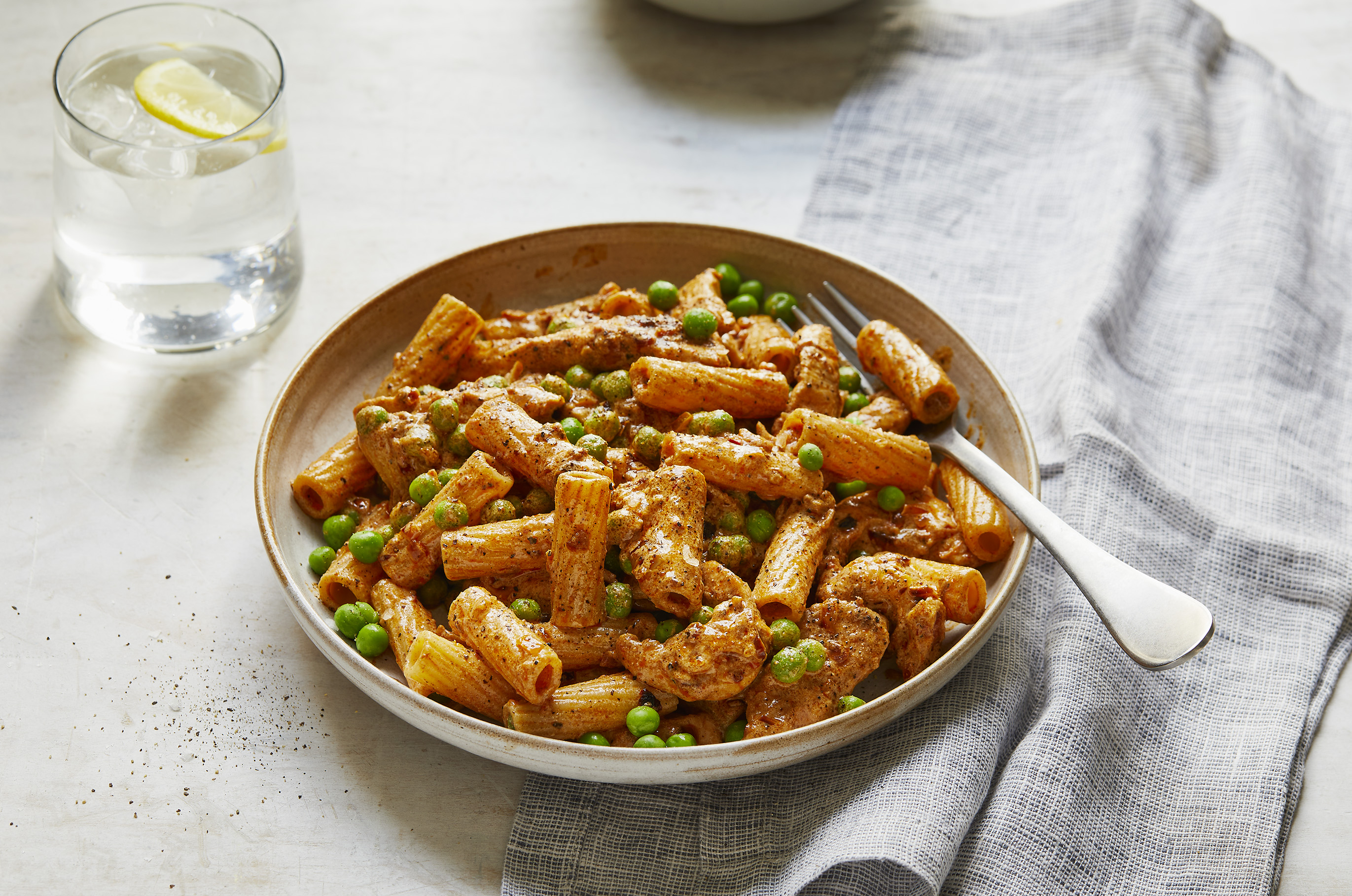 A bowl of creamy cajun chicken pasta alongside a glass of water with lemon.