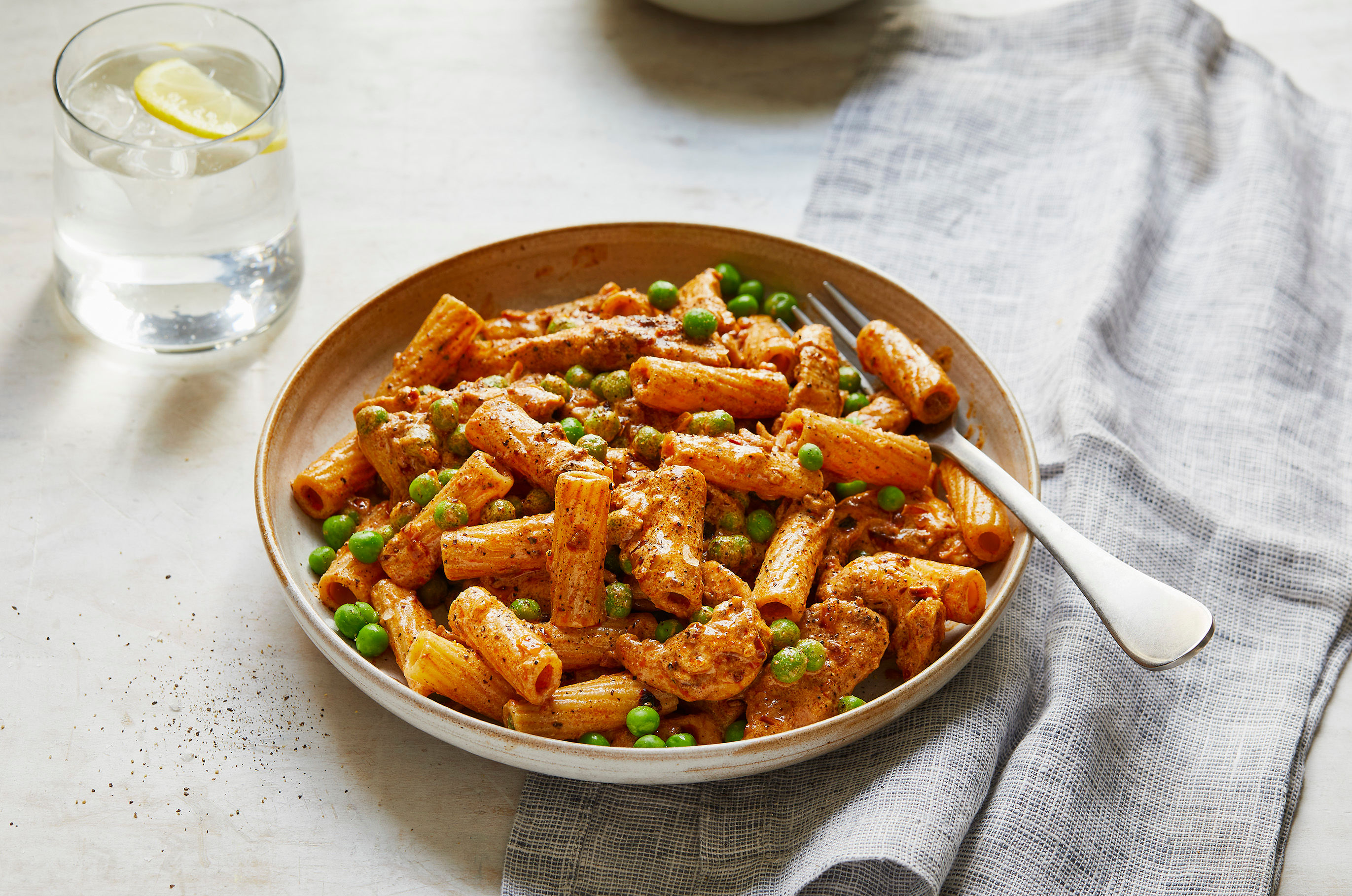 A bowl of creamy cajun chicken pasta alongside a glass of water with lemon.