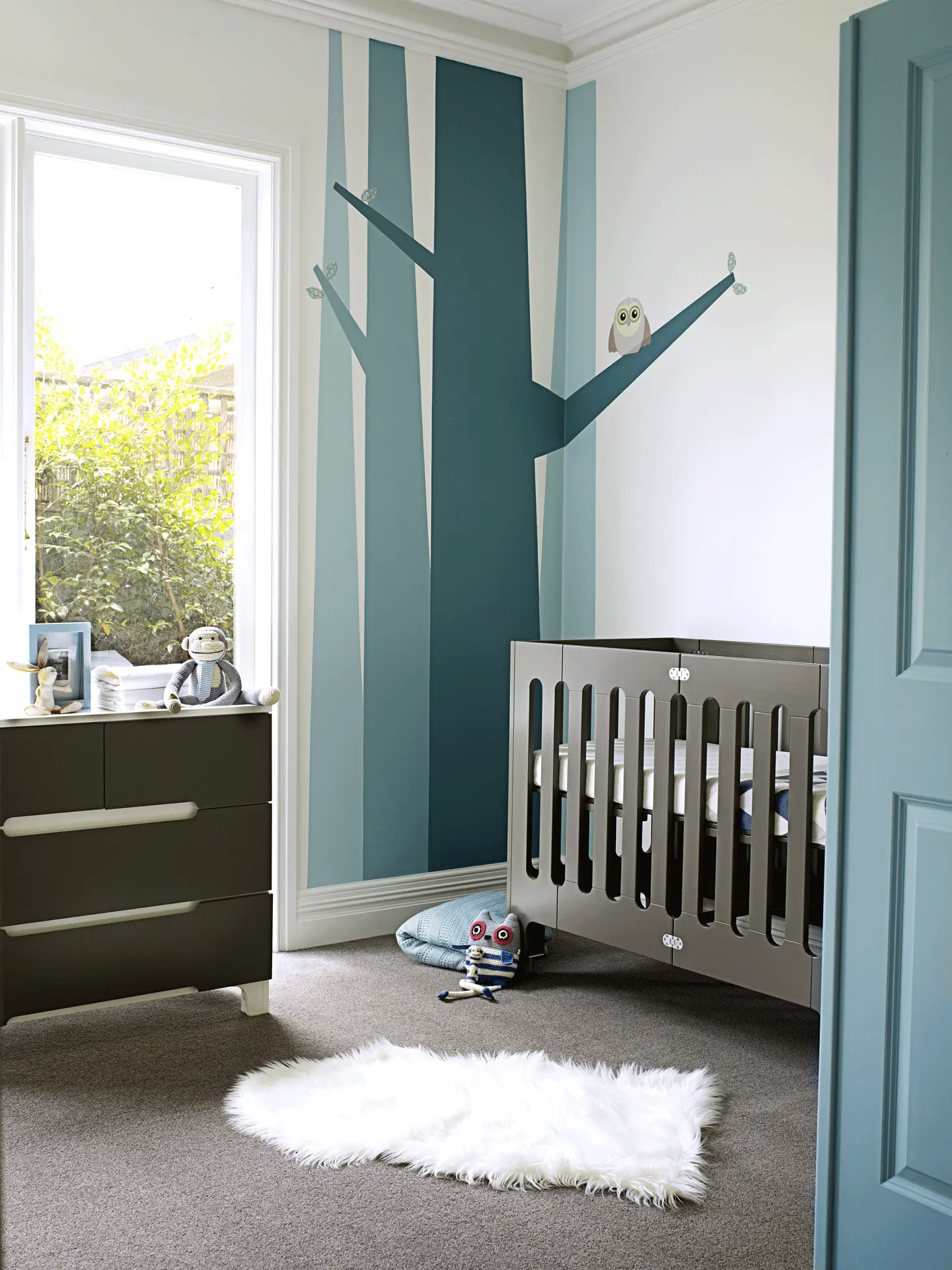 White nursery with blue painted feature wall and charcoal cot and drawers