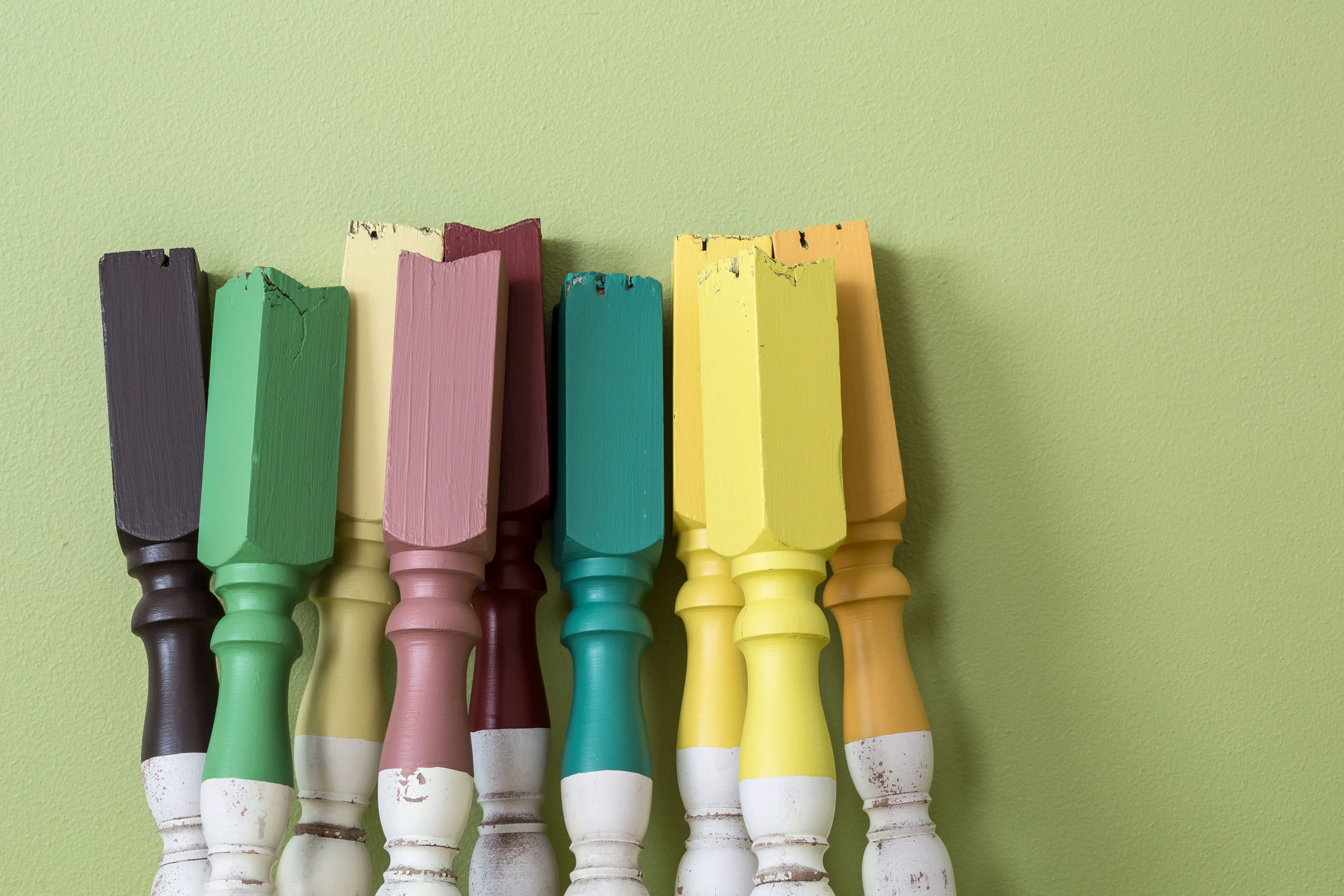 Old white balustrade posts with ends in different colours leaning against green wall. Colour Forecast 2013 - Seek 