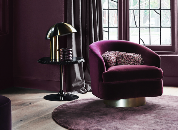 A modern velvet purple armchair is well-suited to this living room with heavy drapes and deep purple walls. 
