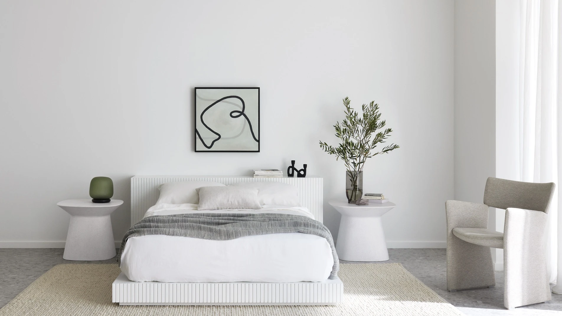 Bed and bedside tables against wall with artwork featured. Small chair beside window. 