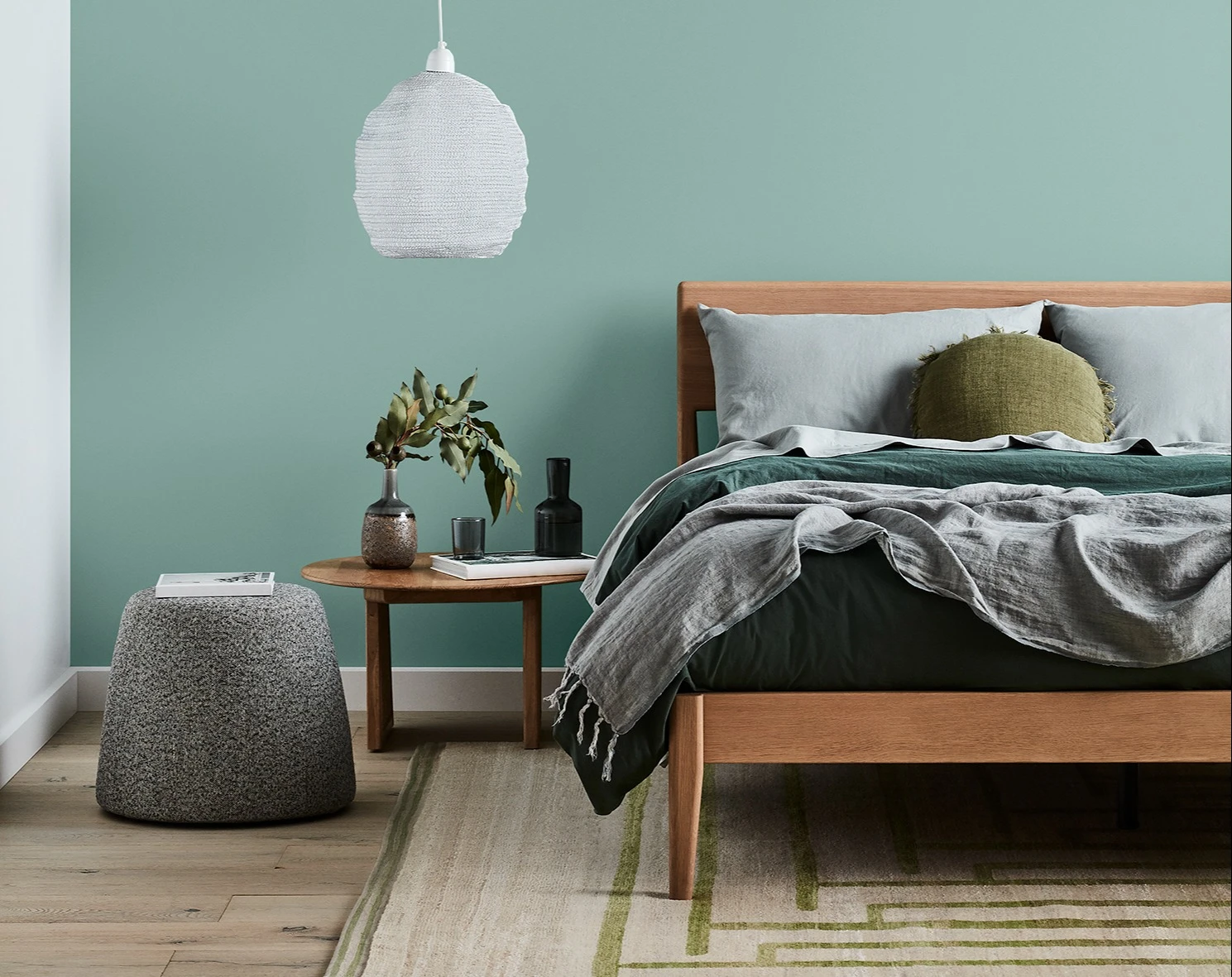 Green themed bedroom with bed, hanging lamp and bedside table to left.