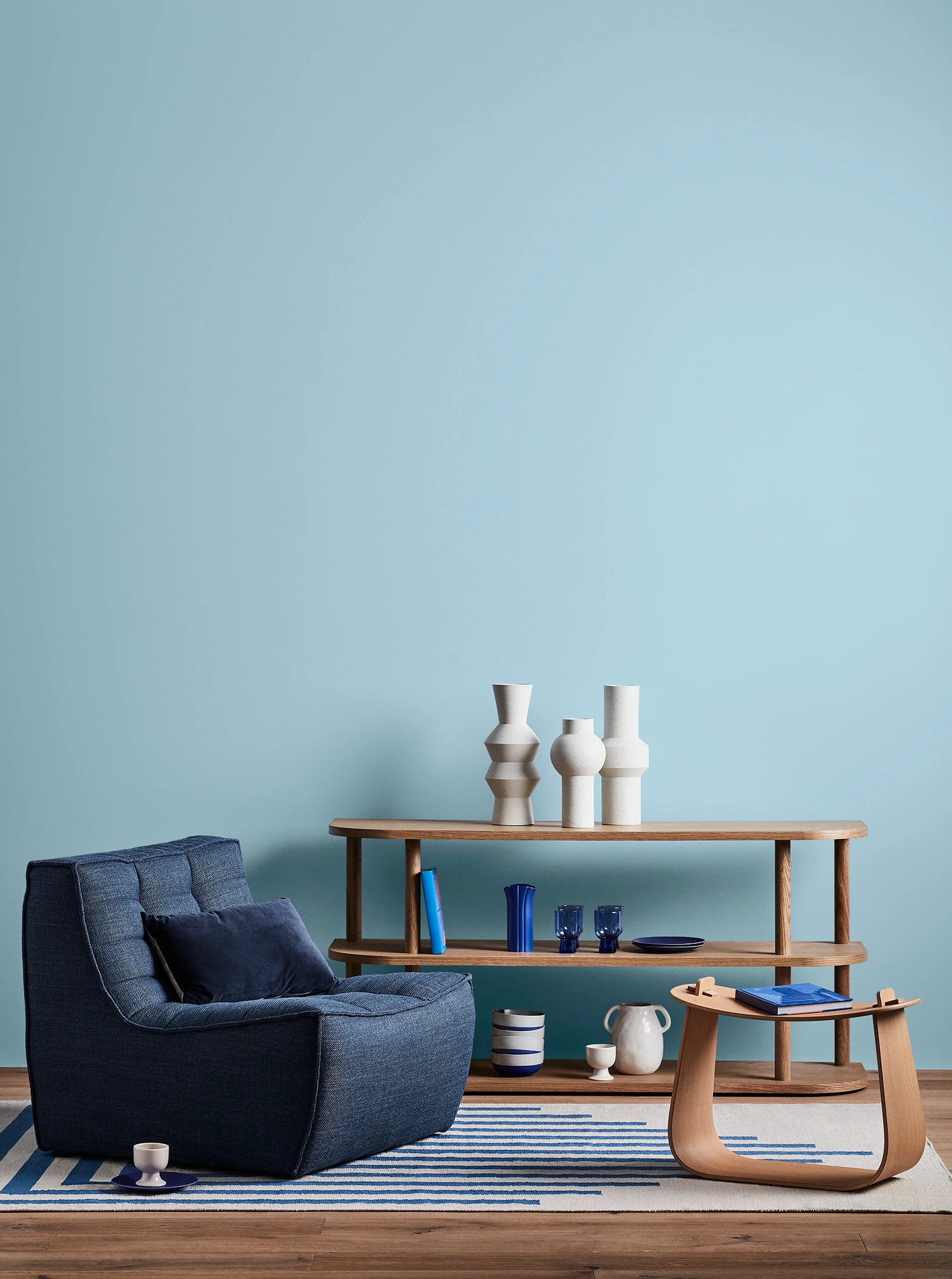 Blue living room with blue armchair, wooden coffee table and shelves with blue and white decor.