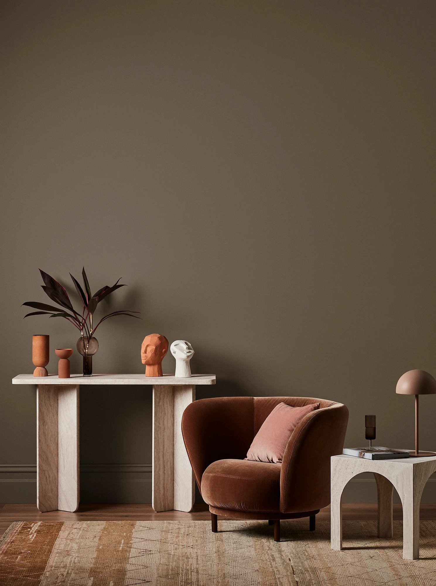 Brown living room with white console table with terracotta and white decor, velvet brown armchair and neutral side table with brown lamp.