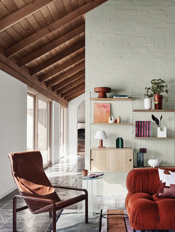 Brown chair in living room with light green brick wall and wooden sloped ceiling looking down hallway