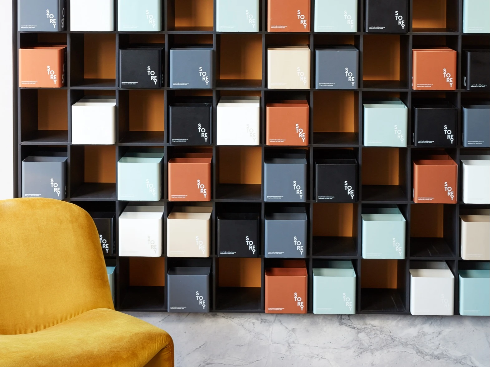 deep yellow chair in front of wall featuring cubes in white, black, cream, light green and orange.