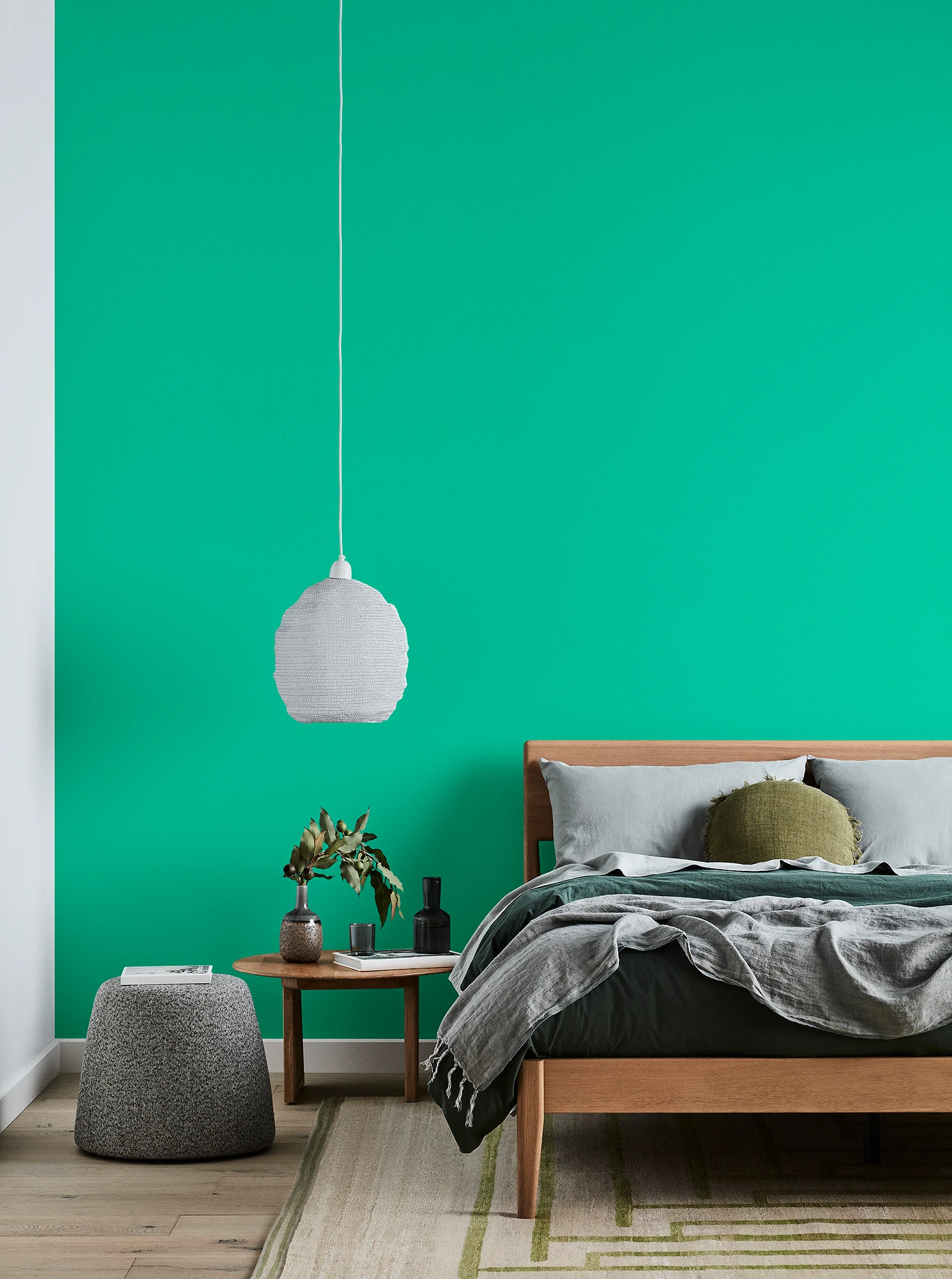 Green bedroom with timber bed and side table, white pendant light and grey linens.